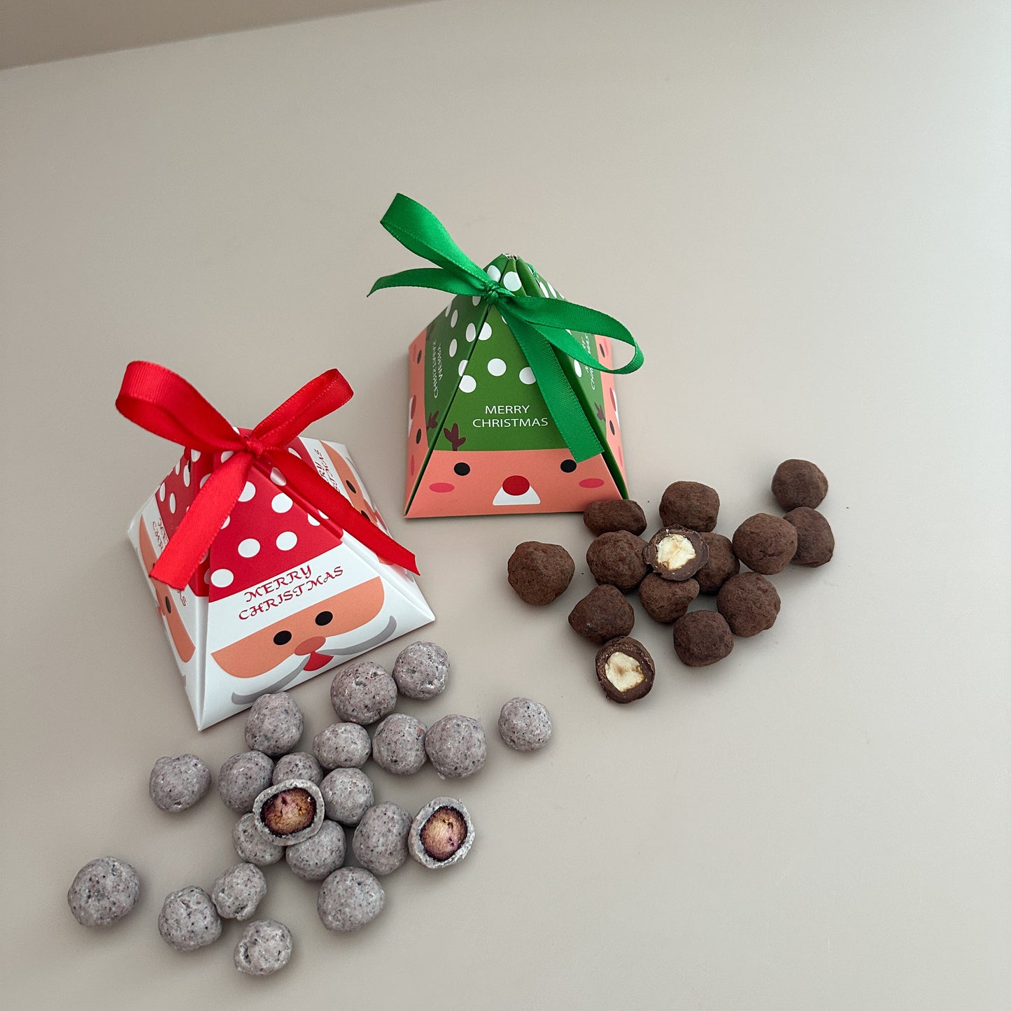 Two small gift boxes with red and green ribbons and a pile of chocolate truffles on a light surface.