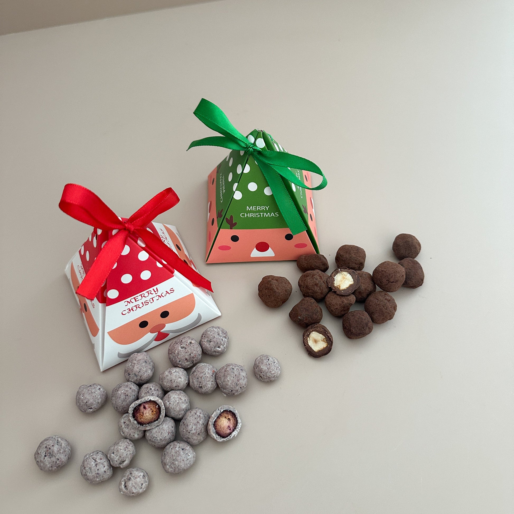 Two small gift boxes with red and green ribbons and a pile of chocolate truffles on a light surface.