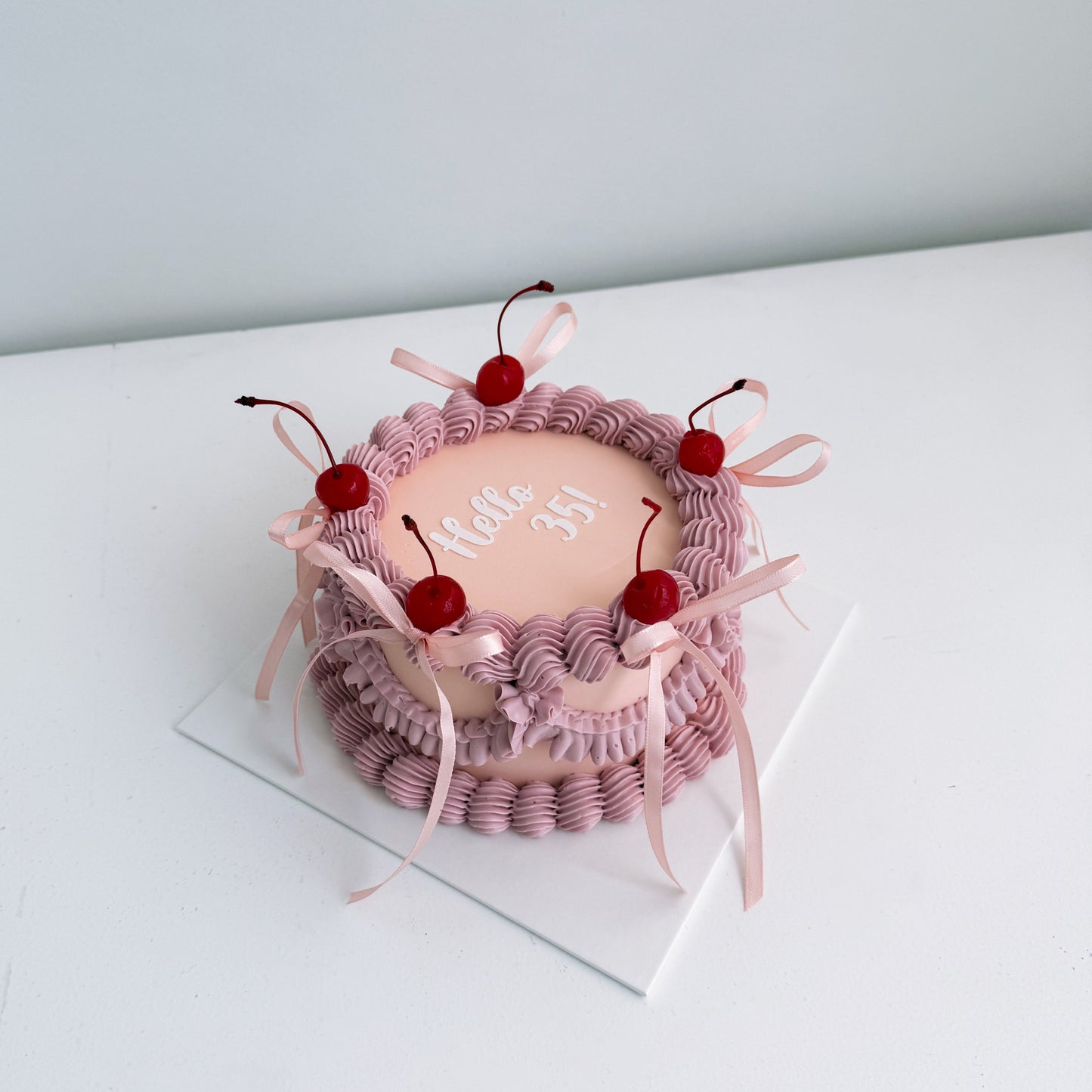 Small pink cake with red cherries on a white surface 