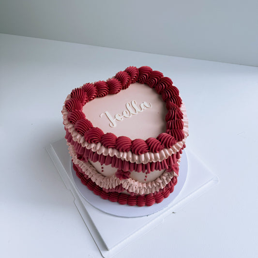 Heart-shaped cake with red and pink ruffled design on a white surface